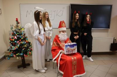 Święty Mikołaj z dwoma aniołkami i diabełkiem pozują do zdjęcia.