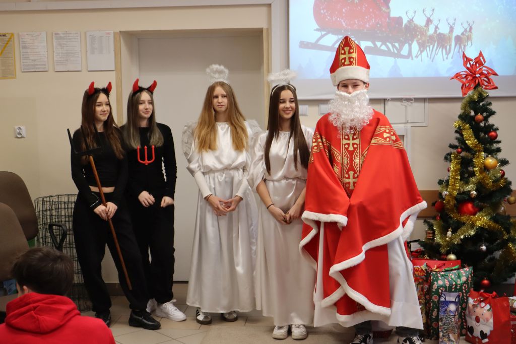Święty Mikołaj z dwoma aniołkami i diabełkiem pozują do zdjęcia.