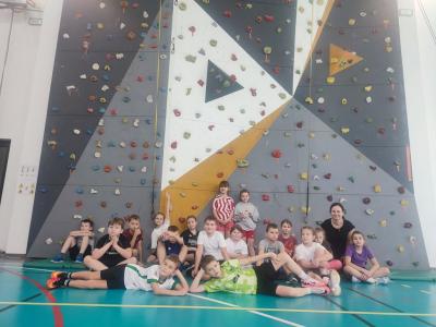 Dzieci biorą udział w zajęciach sportowych w hali sportowej na ściance wspinaczkowej.