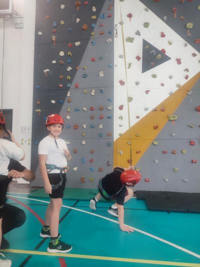 Dzieci biorą udział w zajęciach sportowych w hali sportowej na ściance wspinaczkowej.