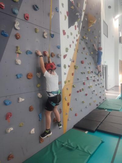 Dzieci biorą udział w zajęciach sportowych w hali sportowej na ściance wspinaczkowej.