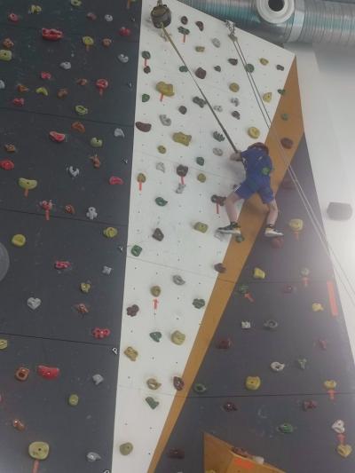 Dzieci biorą udział w zajęciach sportowych w hali sportowej na ściance wspinaczkowej.