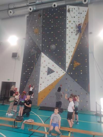 Dzieci biorą udział w zajęciach sportowych w hali sportowej na ściance wspinaczkowej.