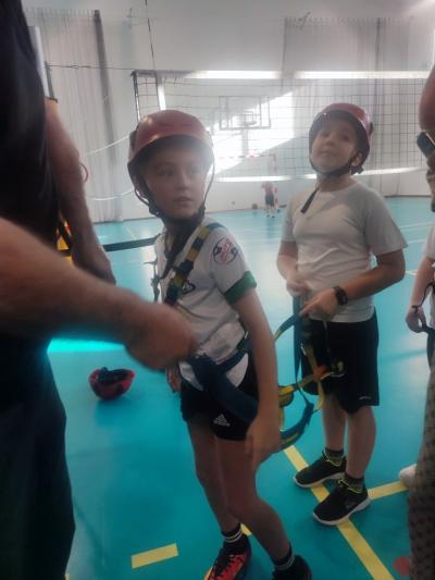 Dzieci biorą udział w zajęciach sportowych w hali sportowej na ściance wspinaczkowej.