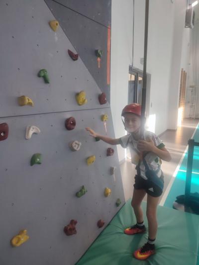 Dzieci biorą udział w zajęciach sportowych w hali sportowej na ściance wspinaczkowej.