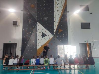 Dzieci biorą udział w zajęciach sportowych w hali sportowej na ściance wspinaczkowej.