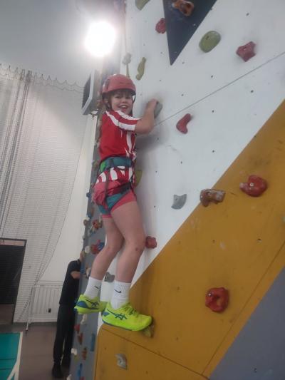 Dzieci biorą udział w zajęciach sportowych w hali sportowej na ściance wspinaczkowej.