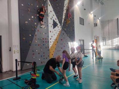 Dzieci biorą udział w zajęciach sportowych w hali sportowej na ściance wspinaczkowej.