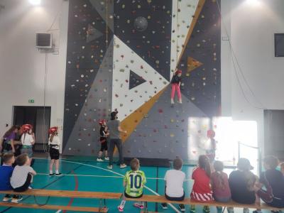 Dzieci biorą udział w zajęciach sportowych w hali sportowej na ściance wspinaczkowej.