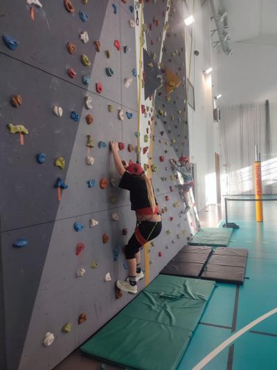 Dzieci biorą udział w zajęciach sportowych w hali sportowej na ściance wspinaczkowej.