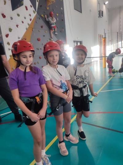 Dzieci biorą udział w zajęciach sportowych w hali sportowej na ściance wspinaczkowej.