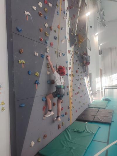 Dzieci biorą udział w zajęciach sportowych w hali sportowej na ściance wspinaczkowej.