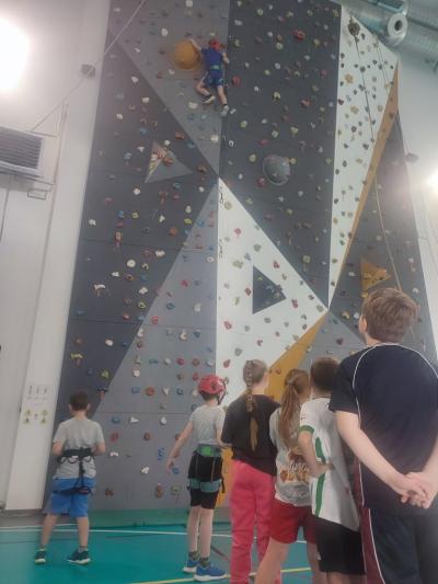 Dzieci biorą udział w zajęciach sportowych w hali sportowej na ściance wspinaczkowej.