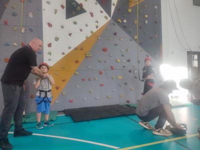 Dzieci biorą udział w zajęciach sportowych w hali sportowej na ściance wspinaczkowej.