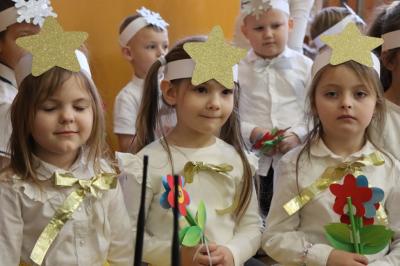 Przedszkolaki stojące przy scenie, śpiewają sto lat, w rękach trzymają upominki dla dziadków