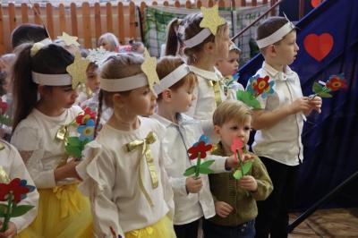 Przedszkolaki stojące przy scenie, śpiewają sto lat, w rękach trzymają upominki dla dziadków