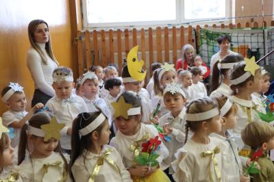 Przedszkolaki stojące przy scenie, śpiewają sto lat, w rękach trzymają upominki dla dziadków