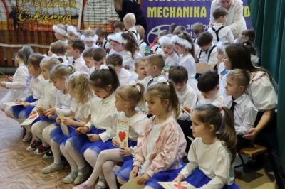 Przedszkolaki stojące przy scenie, śpiewają sto lat, w rękach trzymają upominki dla dziadków