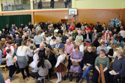 Zdjęcie przedstawia babcie i dziadków siedzących na widowni w hali sportowej