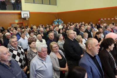 Zdjęcie przedstawia babcie i dziadków siedzących na widowni w hali sportowej