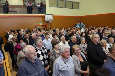 Zdjęcie przedstawia babcie i dziadków siedzących na widowni w hali sportowej