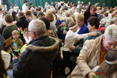 Zdjęcie przedstawia babcie i dziadków siedzących na widowni w hali sportowej