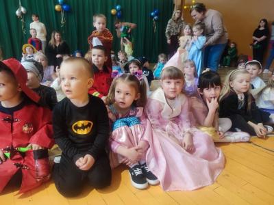 Dzieci w strojach karnawałowych siedzą na parkiecie w hali soprtowej