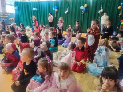 Dzieci w strojach karnawałowych siedzą na parkiecie w hali soprtowej