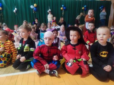 Dzieci w strojach karnawałowych siedzą na parkiecie w hali soprtowej