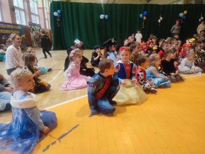 Dzieci w strojach karnawałowych siedzą na parkiecie w hali soprtowej