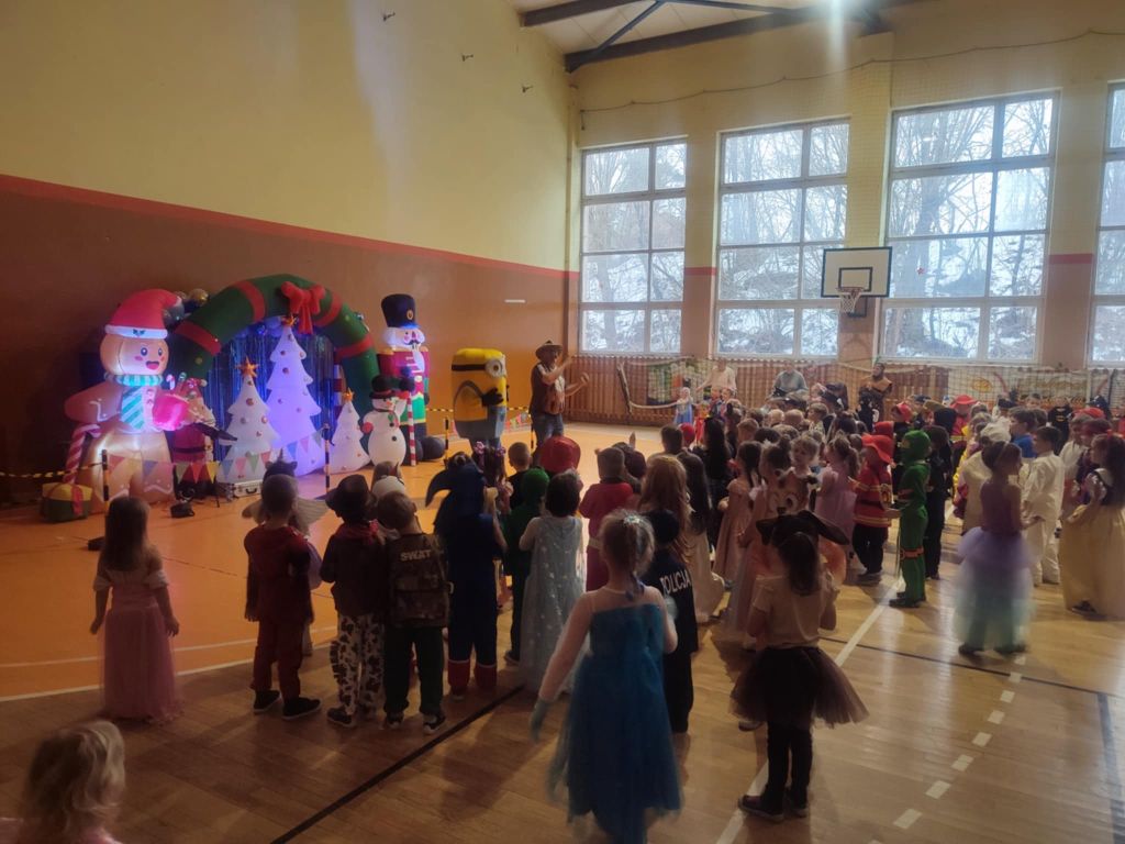 Przedszkolaki tańczą podczas zabawy karnawałowej w hali sportowej