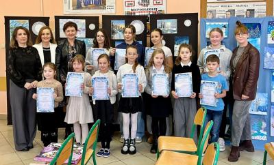 uczniowi z dyplomami i nauczyciele na tle prac