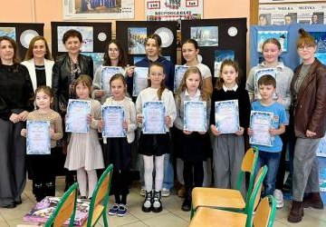 uczniowi z dyplomami i nauczyciele na tle prac