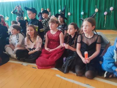 Dzieci w strojach karnawałowych siedzą na parkiecie w hali sportowej