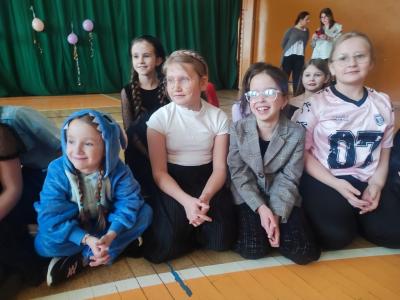 Dzieci w strojach karnawałowych siedzą na parkiecie w hali sportowej