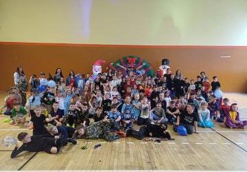 Uczniowie klas 1-3 wraz z opiekunami i wodzirejem na tle pięknej, karnawałowej dekoracji.