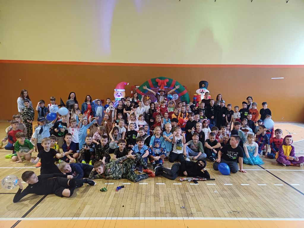 Uczniowie klas 1-3 wraz z opiekunami i wodzirejem na tle pięknej, karnawałowej dekoracji.