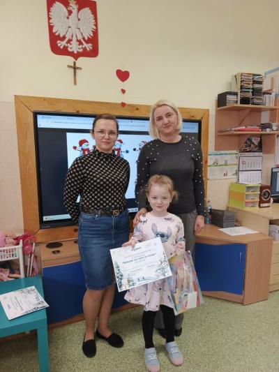 Dziewczynka z grupy misie pozuje do wspólnego zdjęcia z nauczycielkami