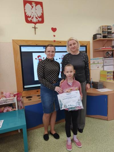 Dziewczynka z grupy misie pozuje do wspólnego zdjęcia z nauczycielkami