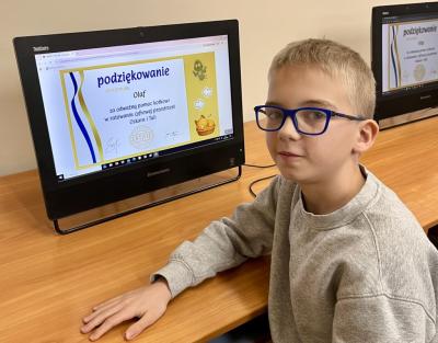 Uczeń pozuje do zdjęcia na tle zbobytego certyfikatu