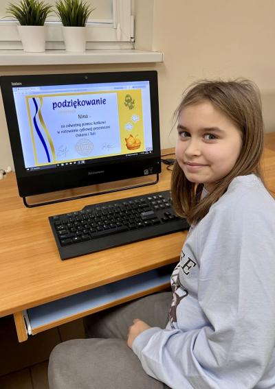Uczennica pozuje do zdjęcia na tle zdobytego certyfikatu