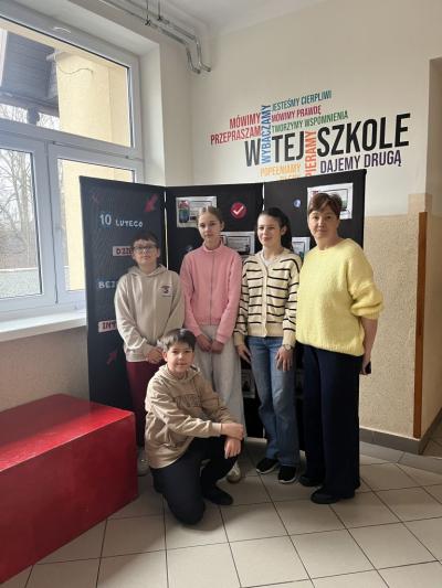 czterech uczniów stoi obok szkolnej gazetki z pnią bibliotekarką