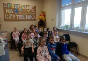 Pierwszoklasiści siedzą na krzesełkach.