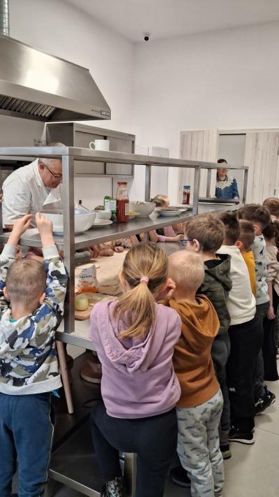 Dzieci obserwują i słuchają pana kucharza podczas robienia pizzy.