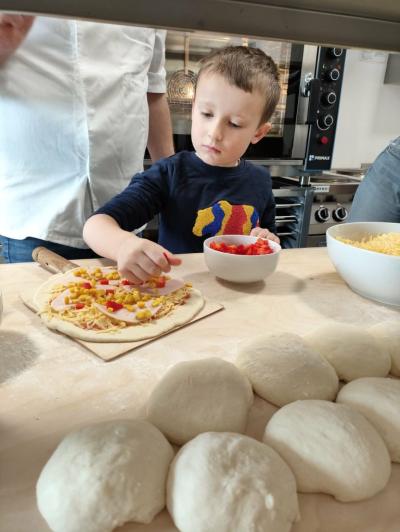 Chłopczyk nakłada na ciasto z serem i szynką paprykę.