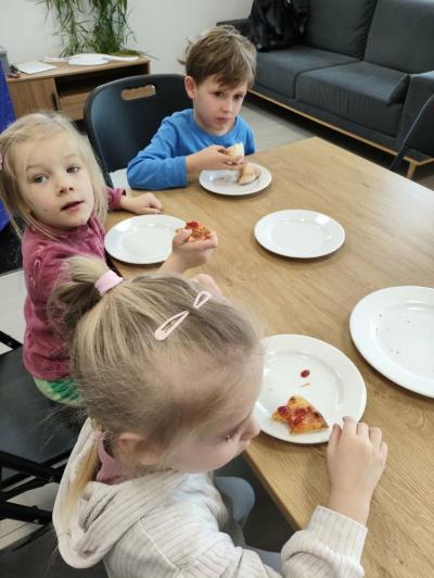 Dwie dziewczynki i jeden chłopczyk siedzą przy stoliku i degustują pizzę.