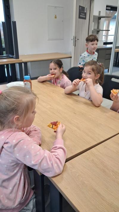 Dzieci degustują przy stoliku wykonaną przez siebie pizze.