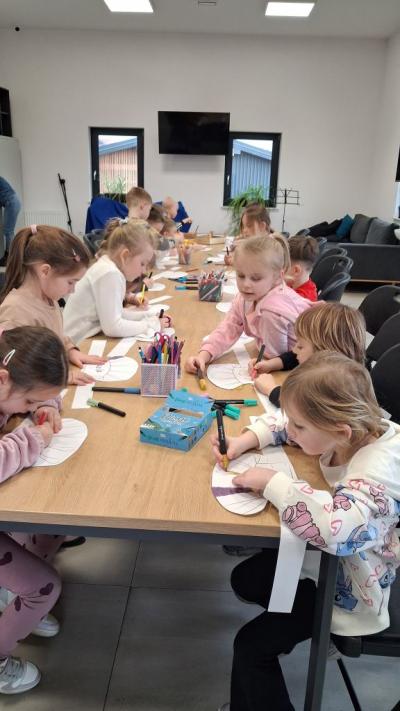 Dzieci kolorują przy stolikach swoje czapki kucharskie