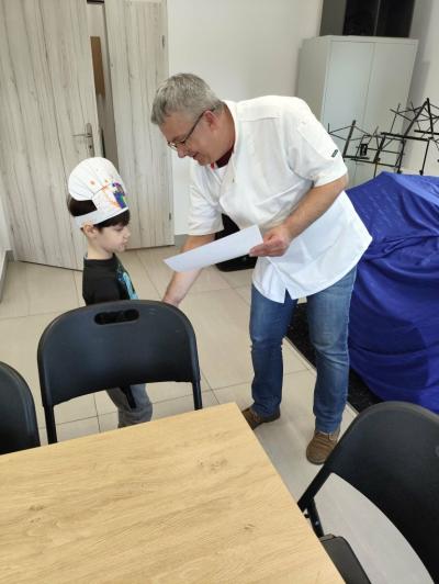 Chłopiec w czapce kucharza otrzymuje certyfikat udziału w warsztatach