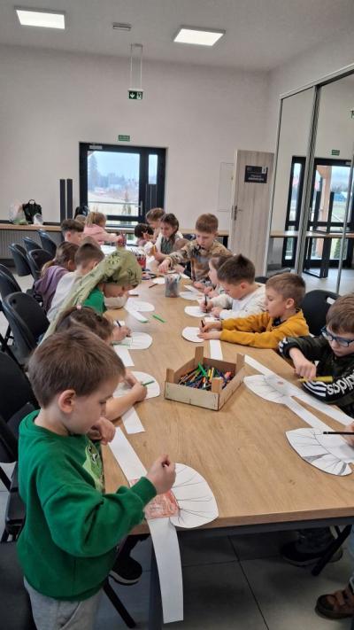 Dzieci kolorują przy stolikach swoje czapki kucharskie.